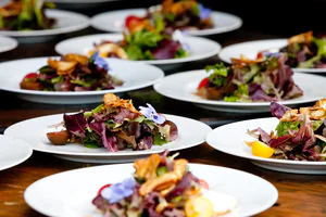 Plated salads with mixed greens, crispy garnishes, and edible flowers arranged on a wooden table.