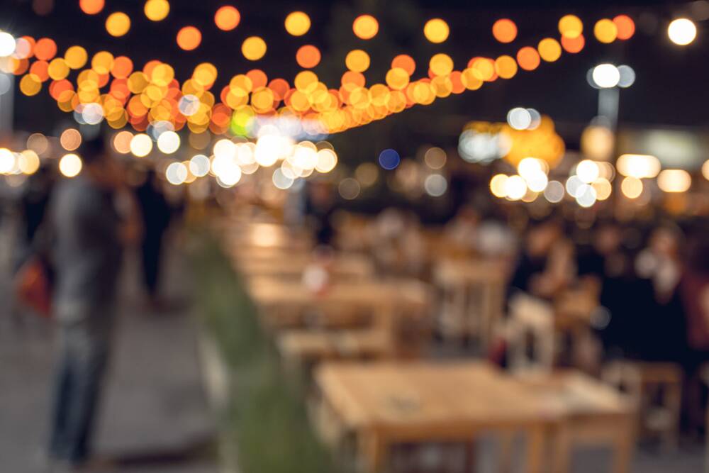 A blurred view of an outdoor evening dining area under a canopy of warm string lights at The Yard in Seneca, SC.