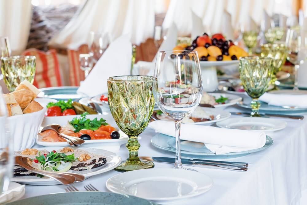A formal dining table set with plates of appetizers, a fruit platter, green and clear wine glasses, cutlery, and napkins.