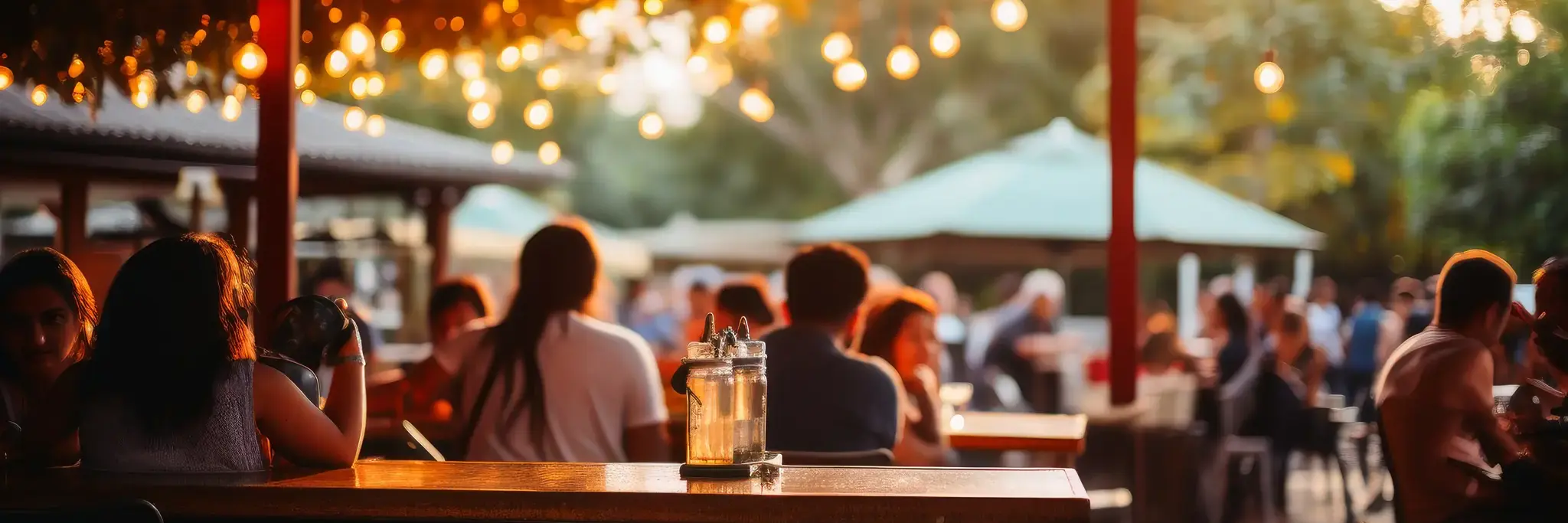 Adobestock 650897144 Outdoor patio dining area at The Yard in Seneca, SC with people seated at wooden tables under a canopy of string lights during warm evening light.